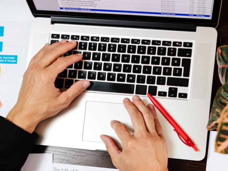 Overhead view of hands on a laptop keyboard with a red pen resting beside the trackpad